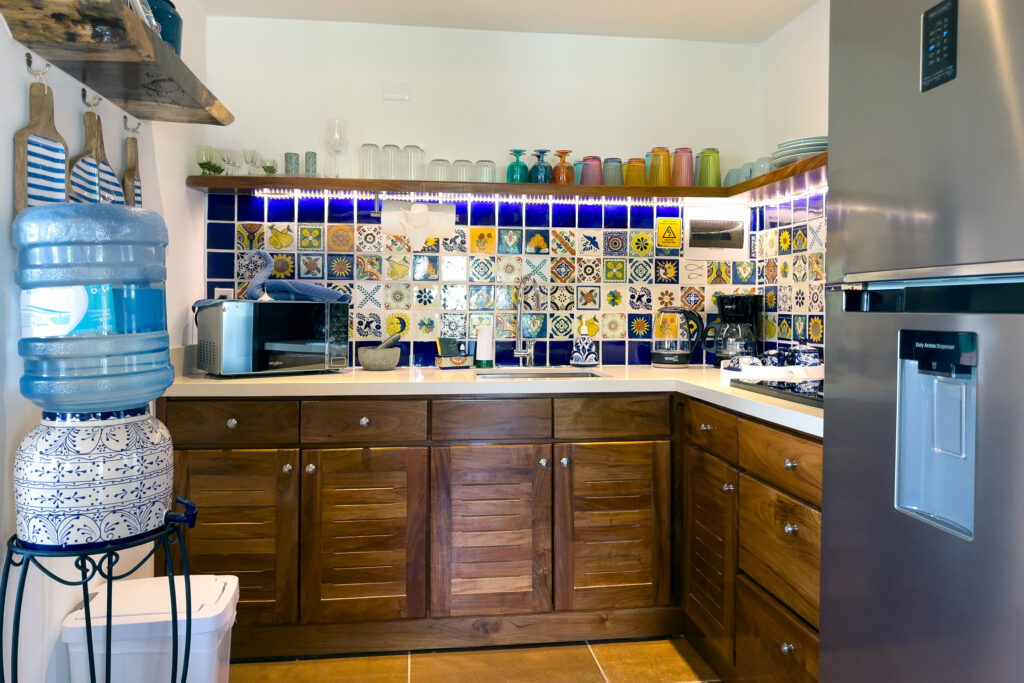 Corner kitchen with patterned tile backsplash, wooden cabinets, microwave, and stainless steel refrigerator.