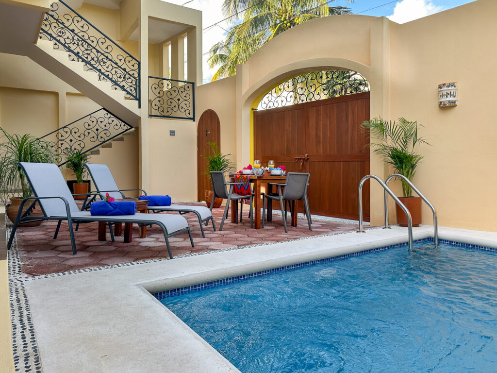 Pool beside reclining chairs and a dining table beneath an arched entrance gate.