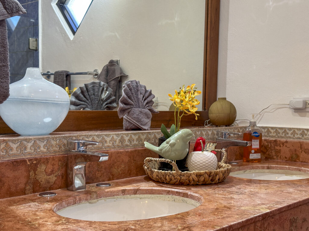 Stone bathroom counter with an inset sink, toiletries, and decorative tray beneath a mirror.