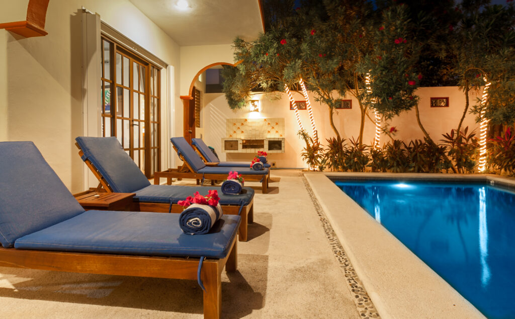 Blue-cushioned lounge chairs with rolled towels beside the illuminated pool.