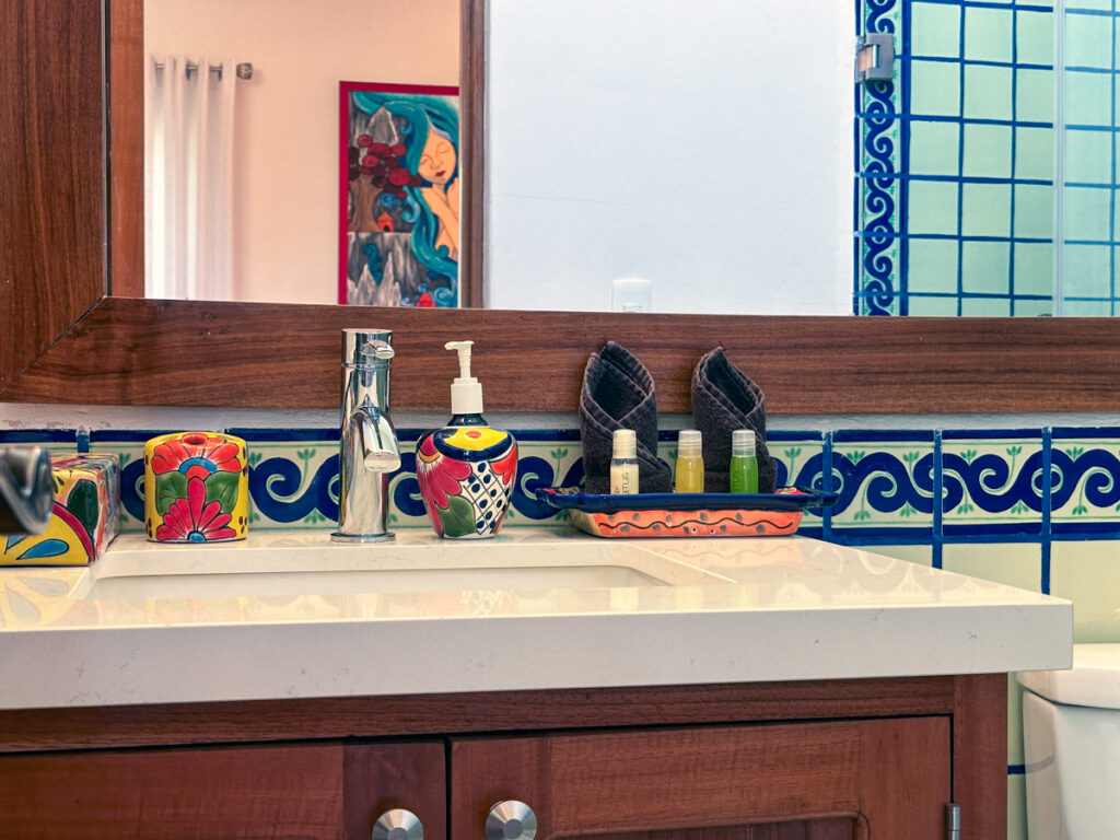 Bathroom sink with colorful ceramic accessories beneath a wooden-framed mirror and blue tile border.