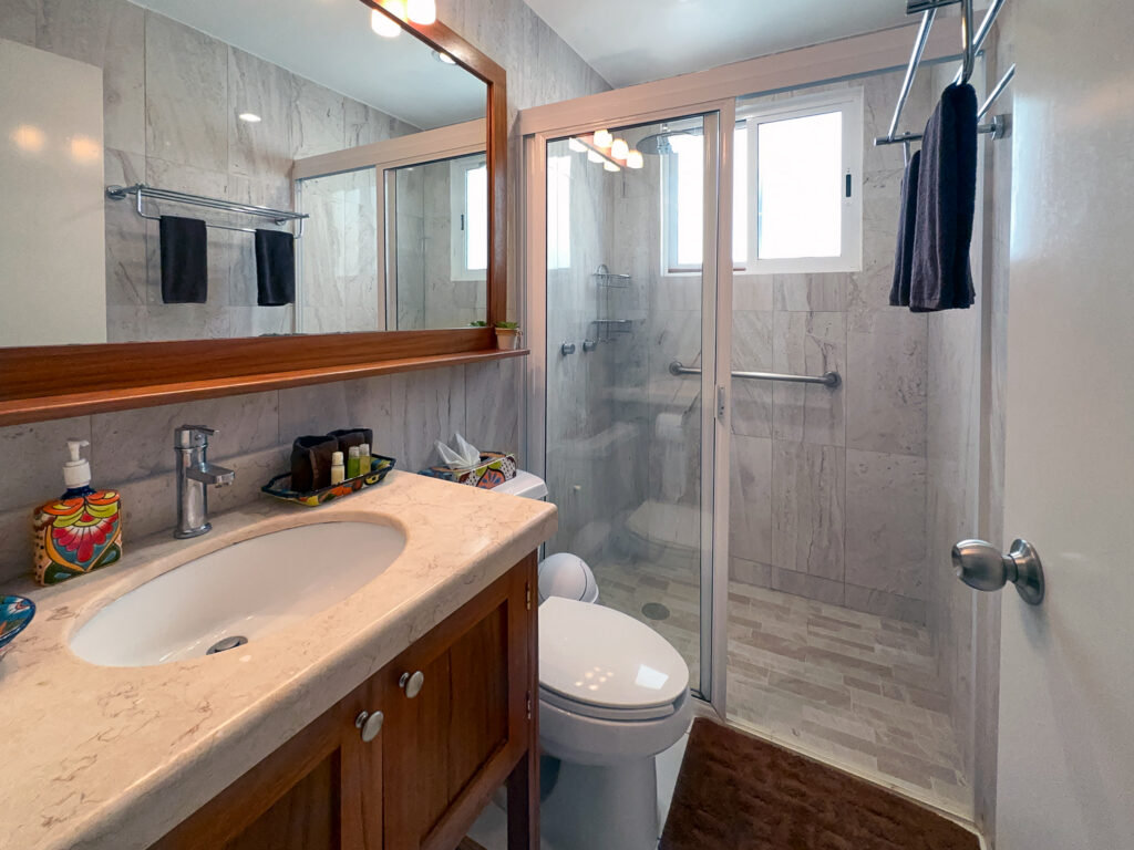 Stone-colored bathroom with wooden vanity, wide mirror, toilet, and glass-enclosed shower.