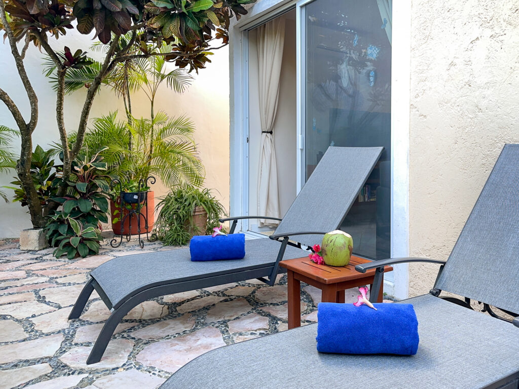 Two gray lounge chairs with rolled blue towels beside a small wooden table and garden plants.
