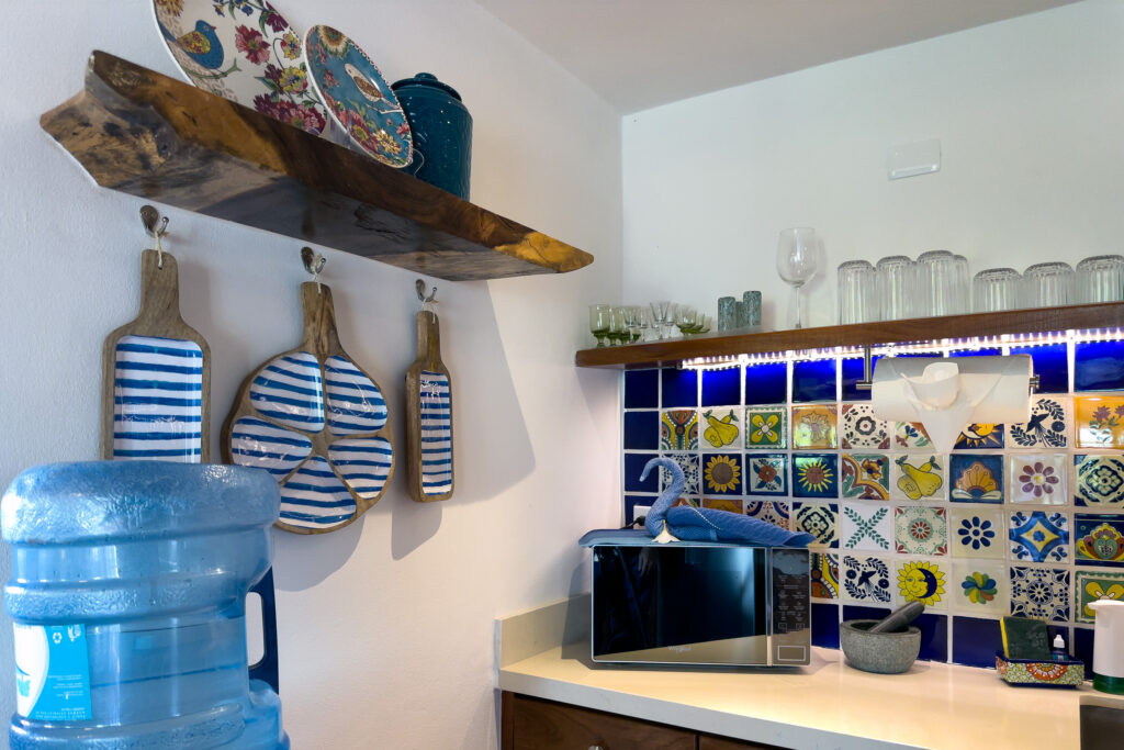 Microwave beneath open shelves, decorative cutting boards, and a colorful tiled backsplash.