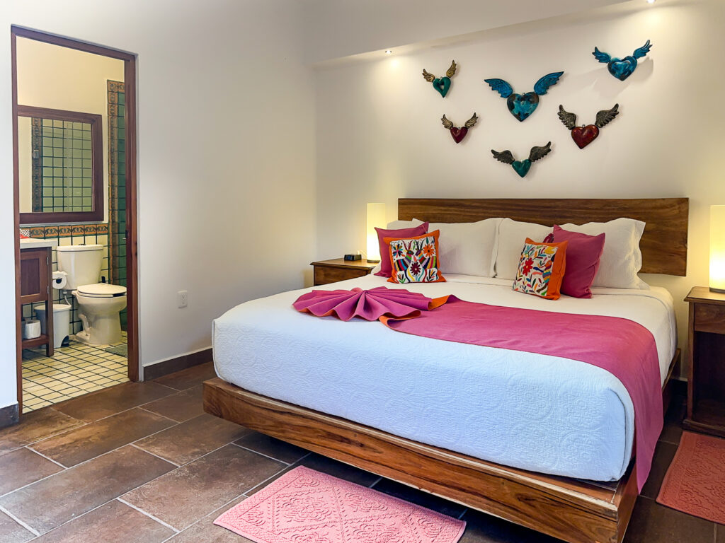 Bed with pink accents beneath decorative birds, with an open bathroom doorway beside it.