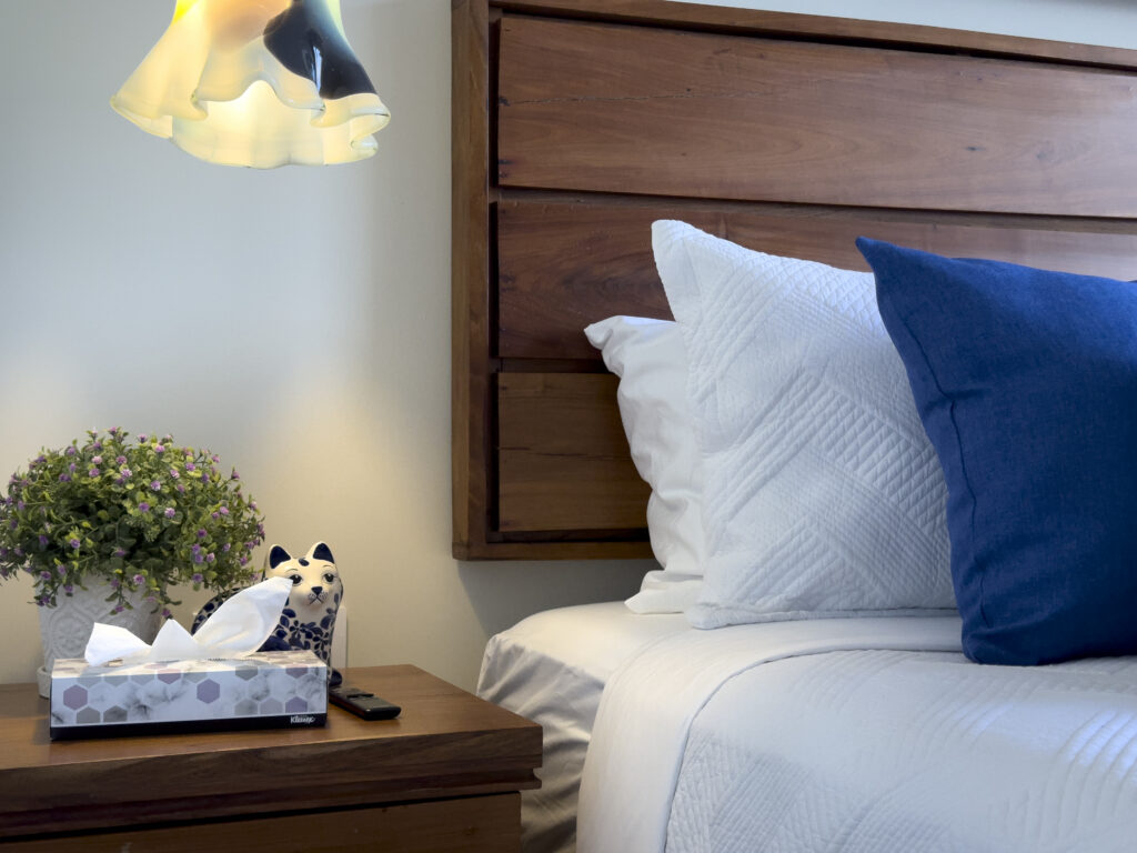 Wooden bedside table with a plant and tissue box beneath a flower-shaped pendant lamp.
