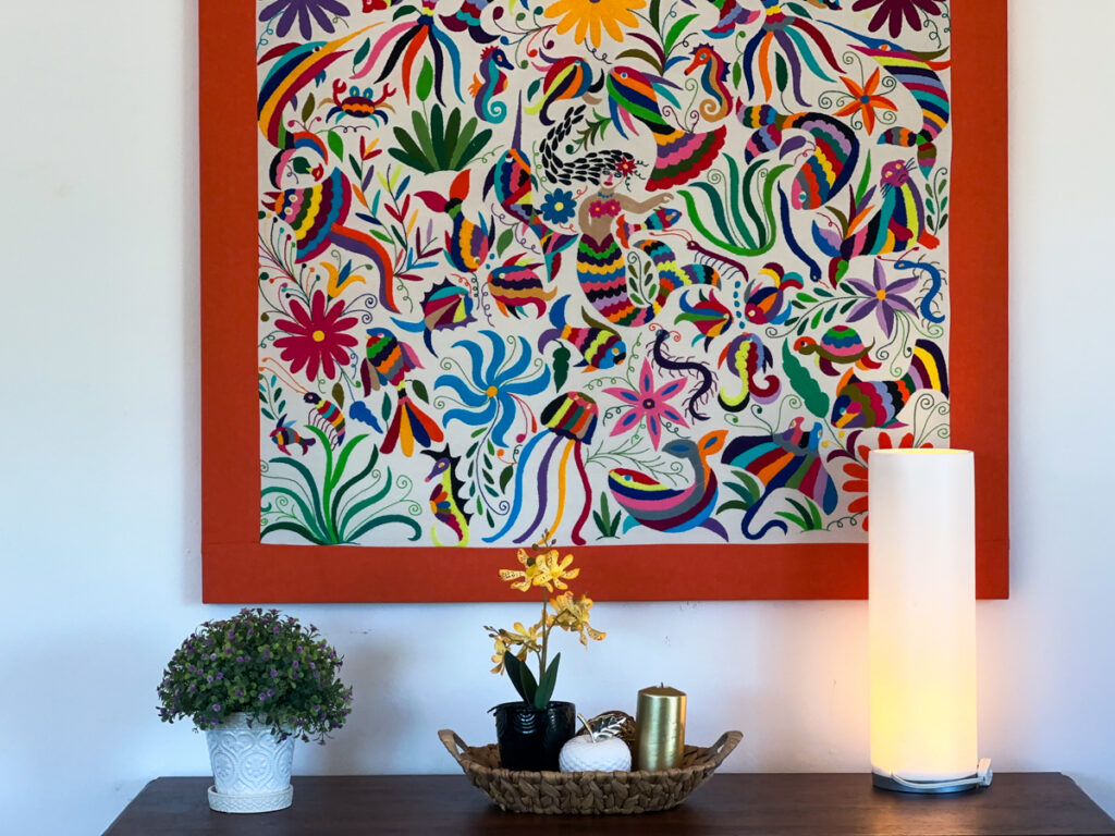 Large colorful floral artwork above a console with a plant, orchid, tray, and lamp.