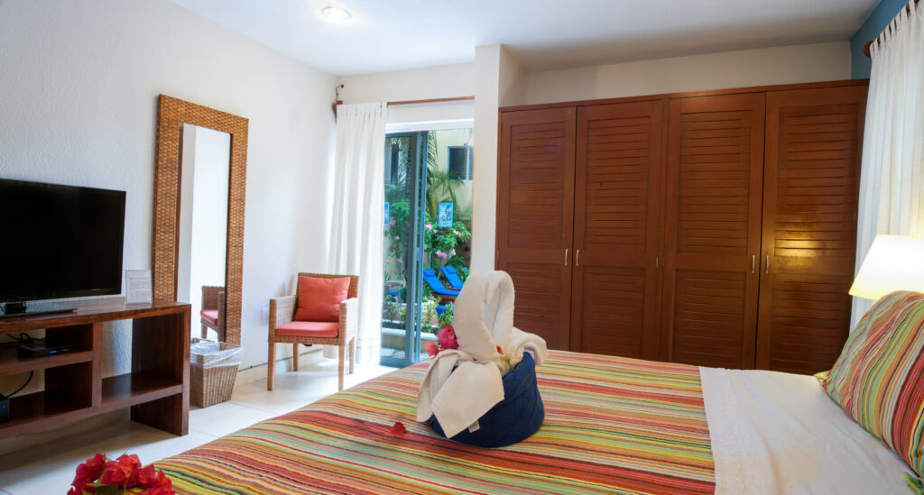 Bed with striped bedding beside wooden closet doors, a television, and a full-length mirror.