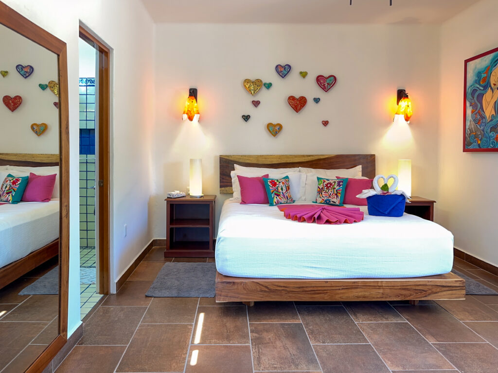 White bed with pink accents beneath colorful heart ornaments and warm wall lamps.