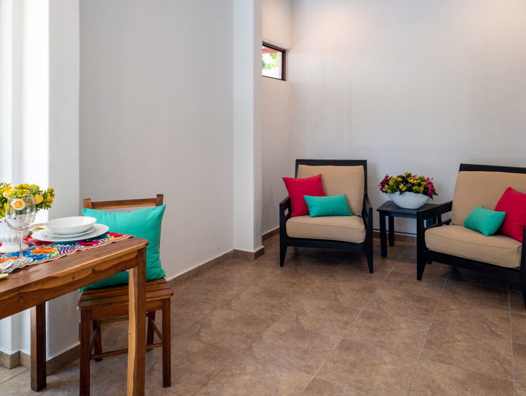 Two armchairs with bright cushions around a small table of flowers beside the dining area.
