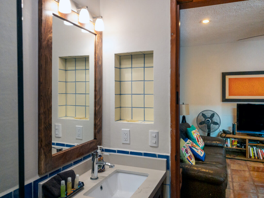 Rectangular sink and wooden-framed mirror beside blue tile trim and a doorway to the lounge.