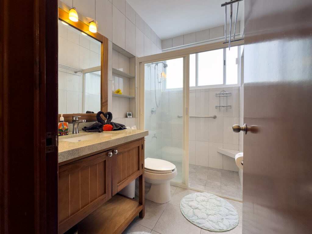 Bathroom with wooden vanity, wide mirror, toilet, and glass shower enclosure.