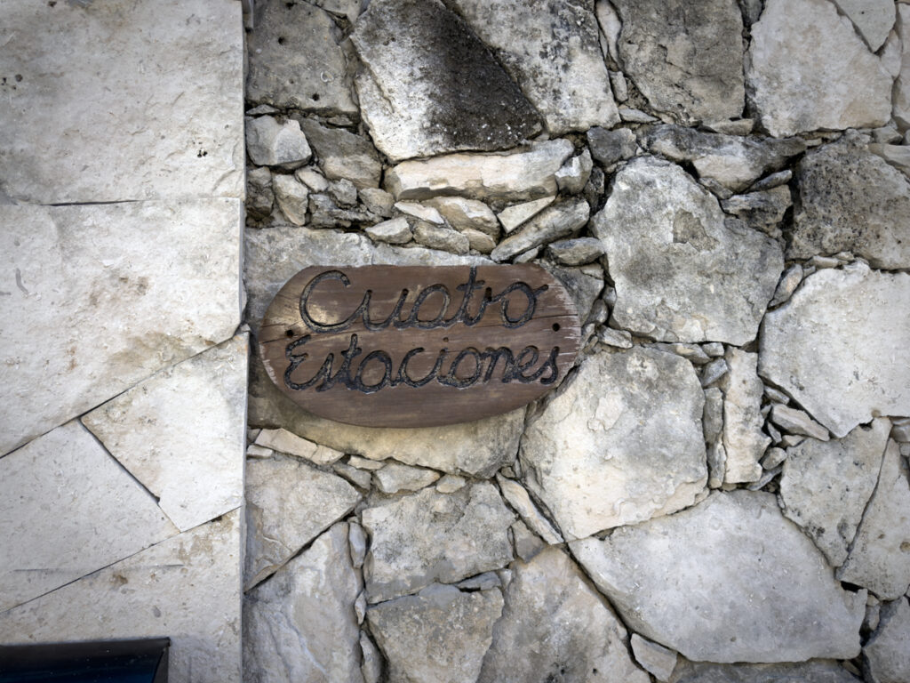 Wooden Cuatro Estaciones plaque mounted on a textured stone wall.