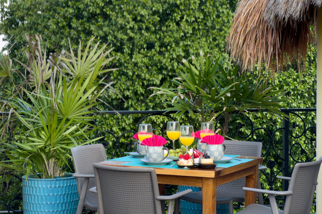 Outdoor table set with dishes and drinks beside terrace railings and dense green foliage.
