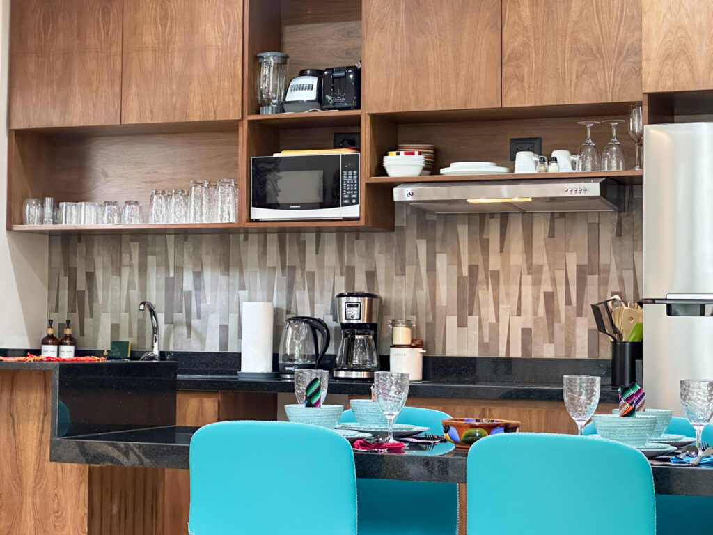 Wooden kitchen shelves with glasses, dishes, and microwave above a counter with small appliances.
