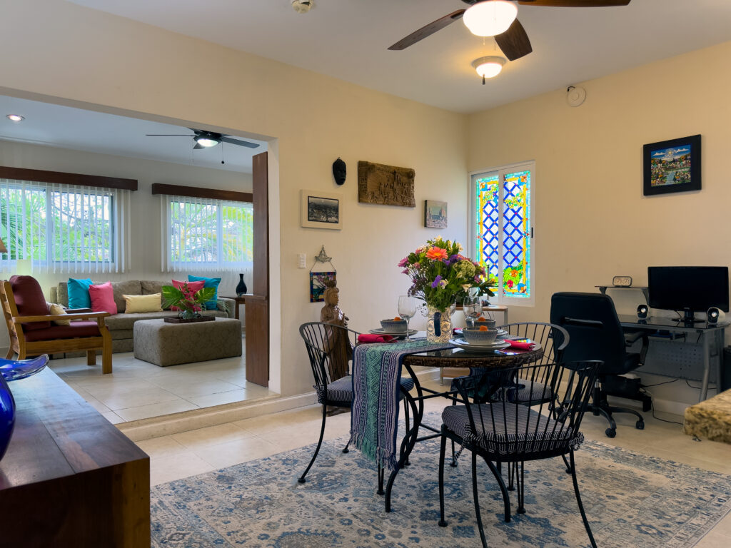 Dining table with flowers beside a computer desk and a wide opening to the sitting room.
