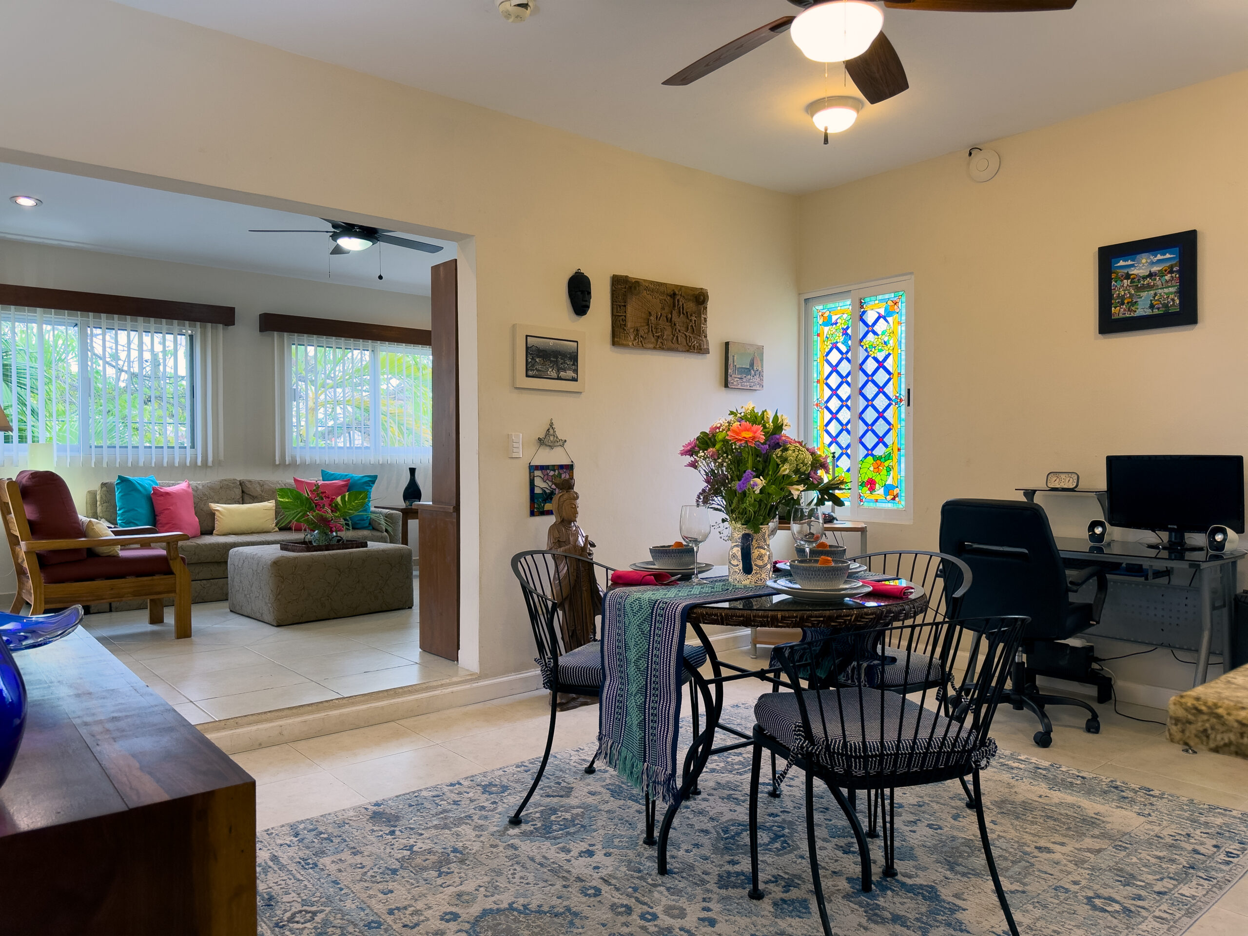 Dining table with flowers beside a computer desk and a wide opening to the sitting room.