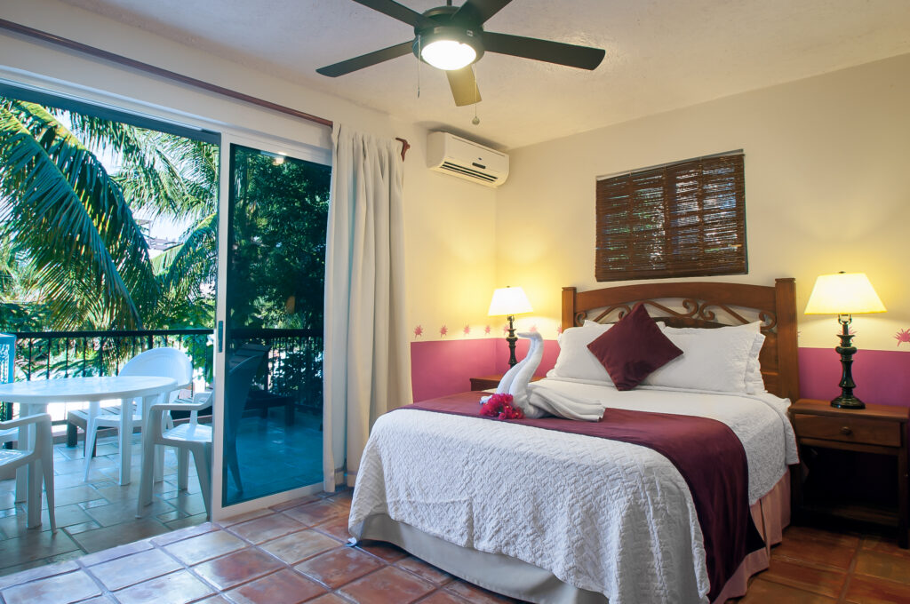 Bed with dark purple accents beside sliding doors to a balcony overlooking palms.