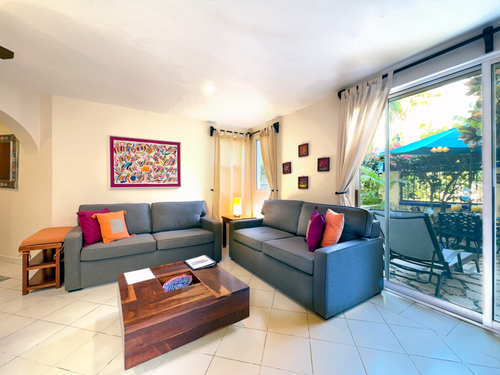 Two gray sofas with colorful cushions around a wooden coffee table beside sliding patio doors.