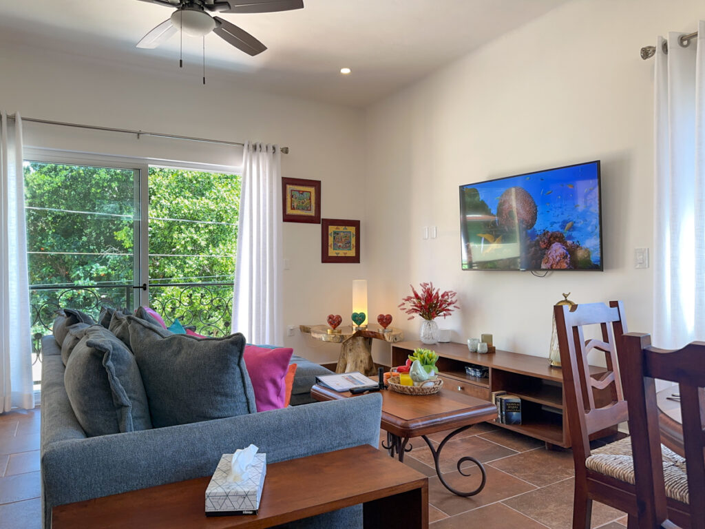 Sectional sofa facing a television and decorative tables near a large window overlooking greenery.