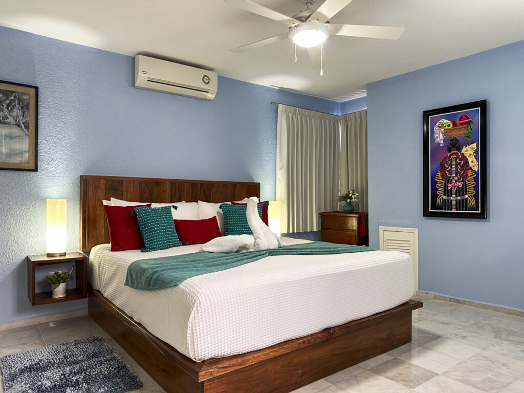 Wooden bed with white bedding and a green throw beneath a ceiling fan in a blue-walled bedroom.