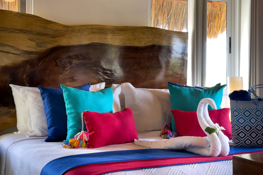 Bed with turquoise, blue, and pink pillows beneath a broad natural wood headboard.