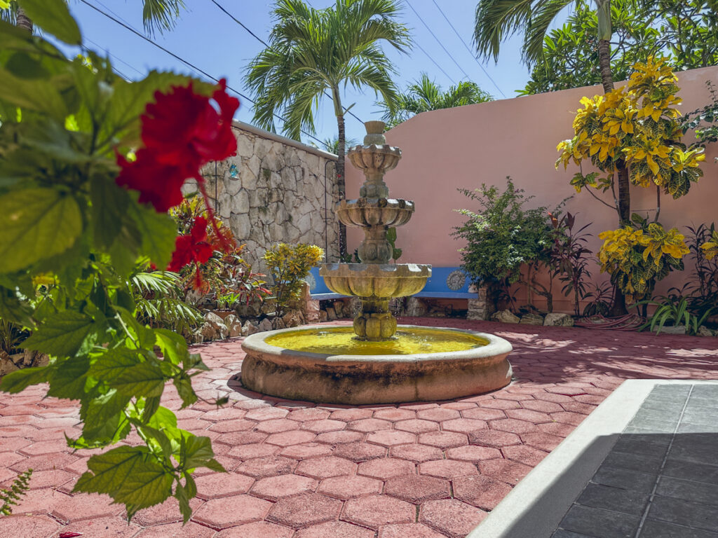 Tiered fountain on a red-paved courtyard surrounded by flowering plants and garden walls.