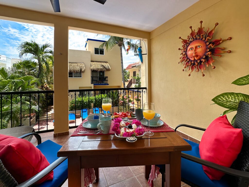 Table set with dishes and drinks on a covered balcony overlooking the pool courtyard.
