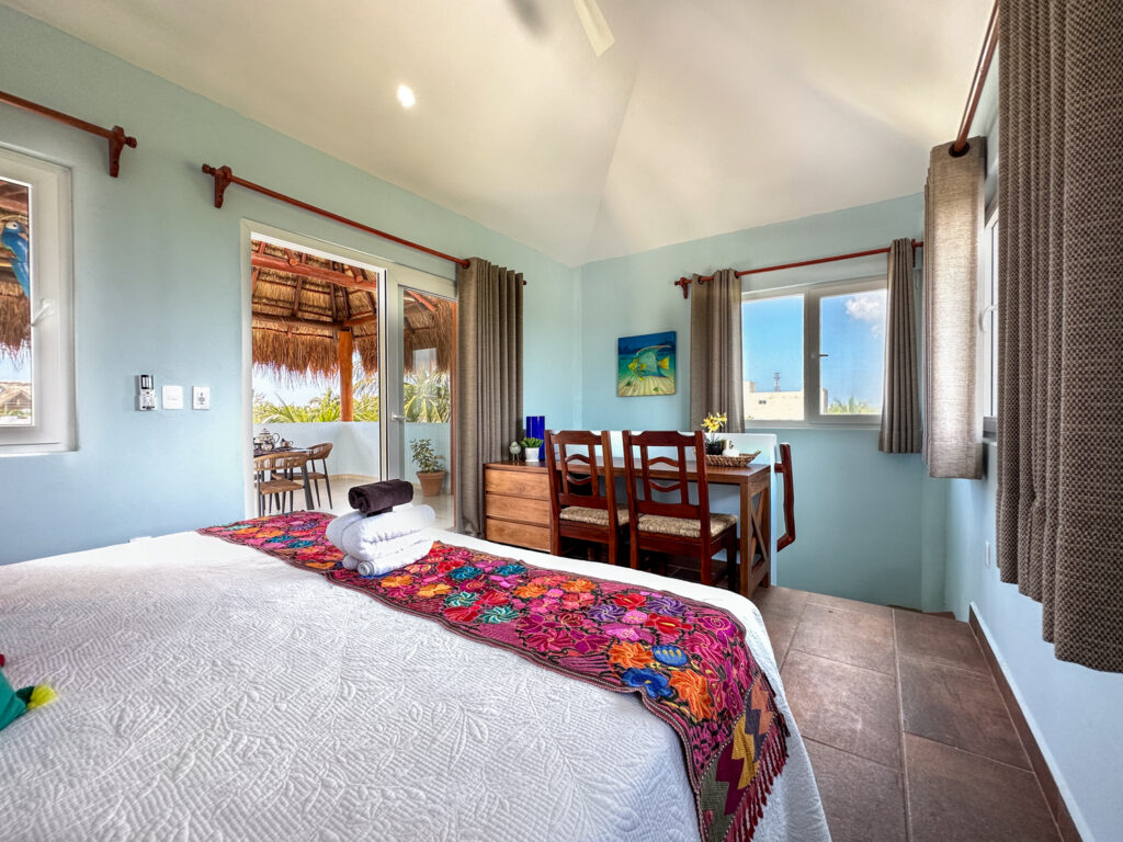 Bed beside a small wooden table and chairs near terrace doors and a large window.