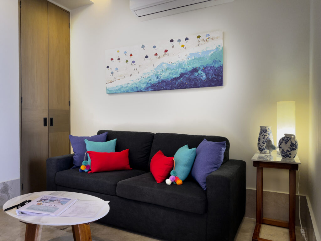 Sofa and round table beneath blue coastal artwork, with wooden storage and a side table.