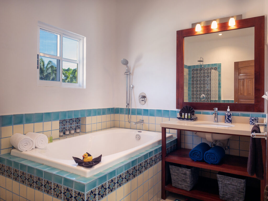 Bathtub with tiled surround beside a wooden vanity and mirror with blue tile accents.