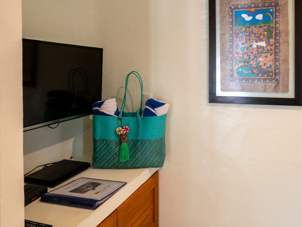 Television and turquoise woven bag on a countertop beneath framed colorful artwork.