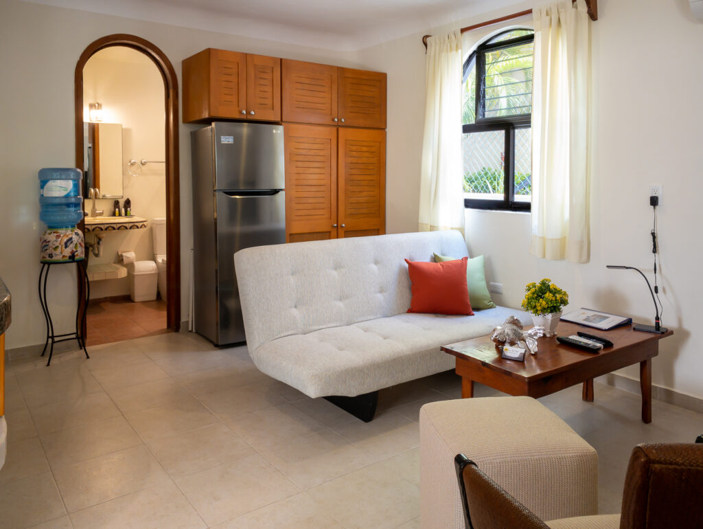 White sofa and wooden coffee table beside a refrigerator, wooden cabinets, and an arched bathroom doorway.