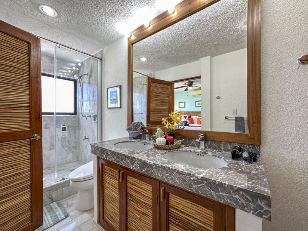 Wooden vanity with gray stone counter beside a glass-enclosed shower and wide mirror.