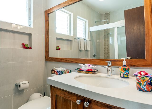 Bathroom sink and wooden vanity beneath a wide mirror reflecting the glass shower enclosure.