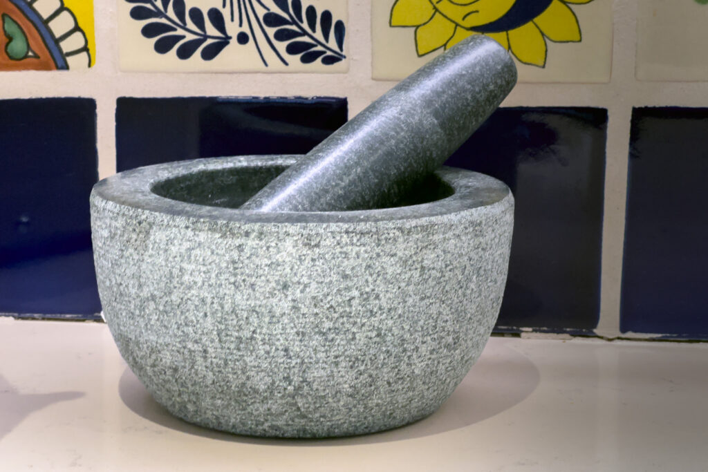 Gray stone mortar and pestle on the kitchen counter beside blue and yellow tiles.