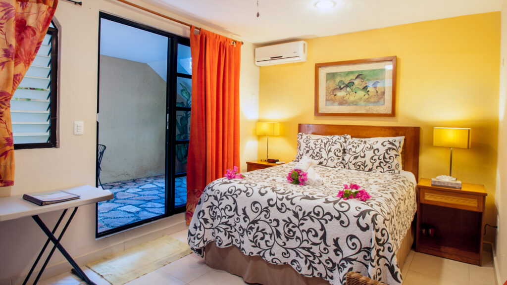 Bed with a black-and-white patterned cover beside orange curtains and a glass patio door.