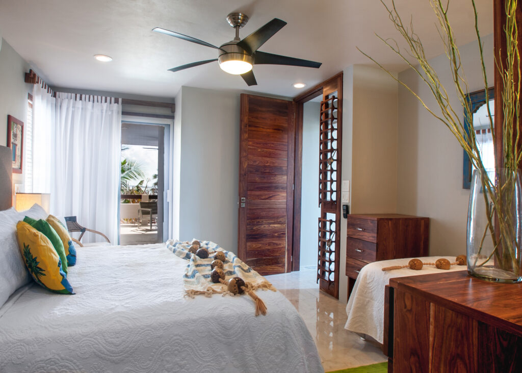 Bed with tropical cushions facing a dresser and glass doors to a covered balcony.