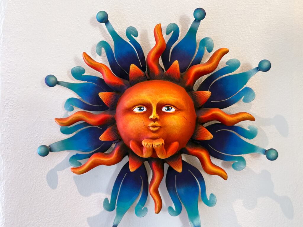 Orange sun face surrounded by blue and orange rays mounted on a pale wall.