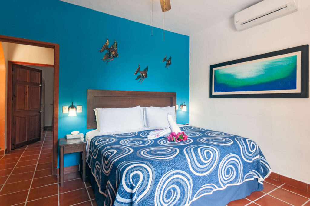Bed with a towel swan beneath small bird wall decorations and framed blue artwork.