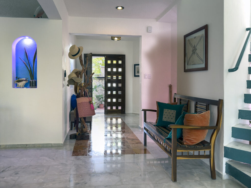 Bright entrance hallway with a cushioned wooden bench, polished floor, and staircase.