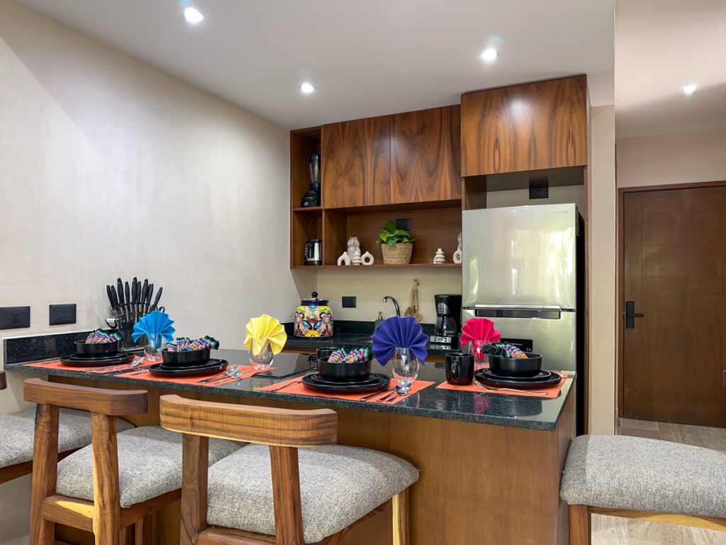 Kitchen island with black dishes and colorful folded napkins surrounded by wooden barstools.