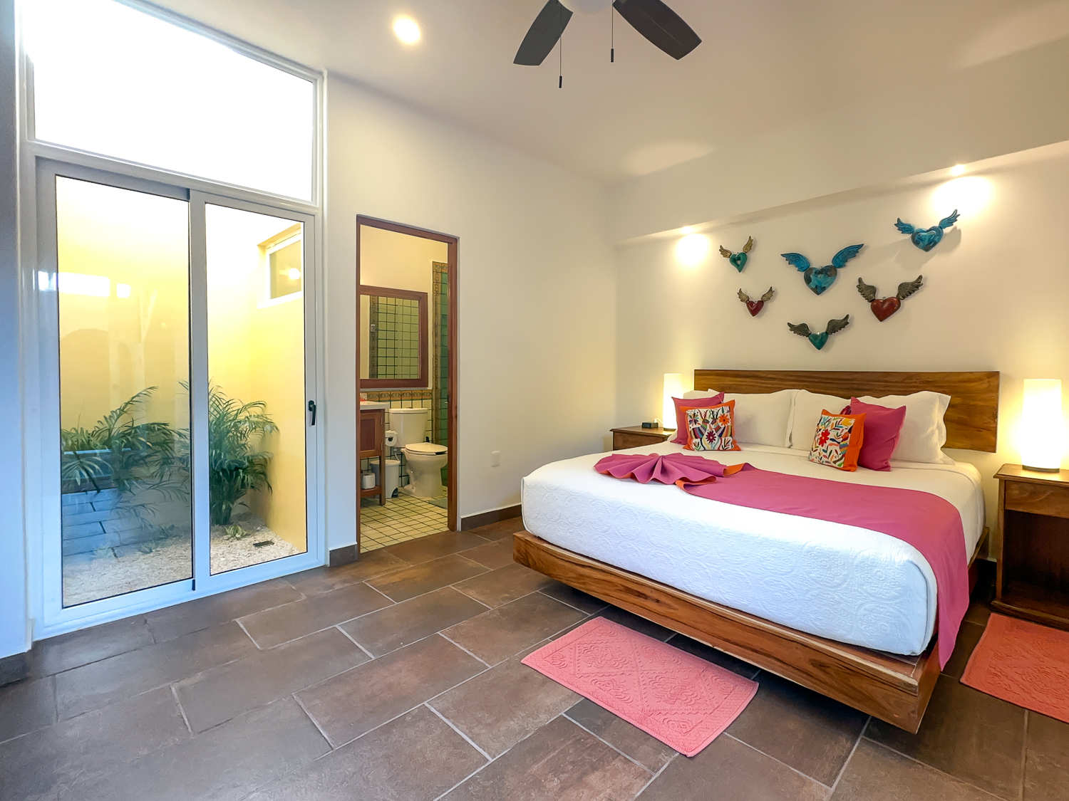 Wooden bed with a pink throw beneath decorative winged hearts beside tall glass patio doors.