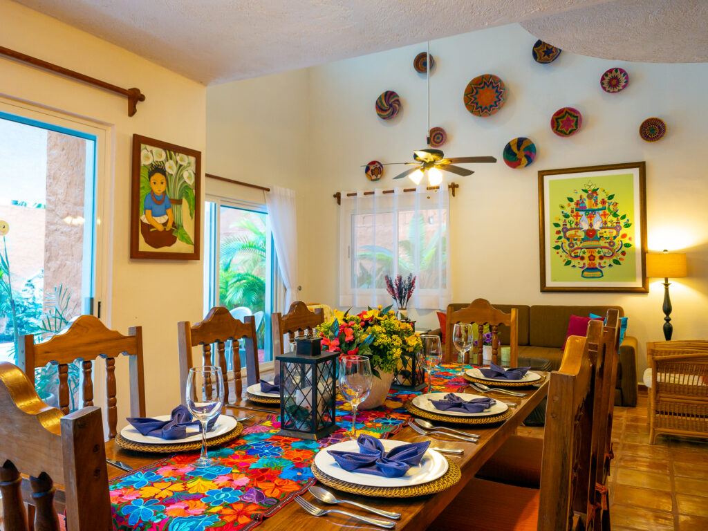 Wooden dining table set with colorful dishes in front of a sofa beneath decorative plates and artwork.