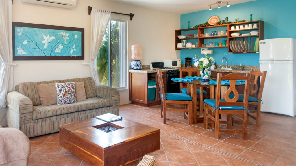 Striped sofa and wooden coffee table beside a dining table and kitchen with turquoise accents.