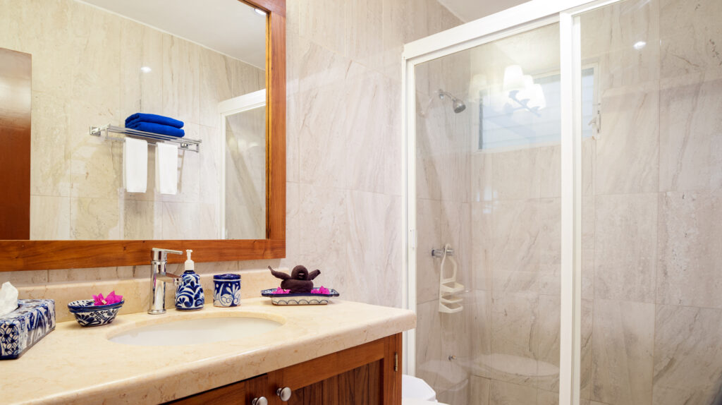 Bathroom with a wide mirror, stone-colored vanity, and glass-enclosed shower.