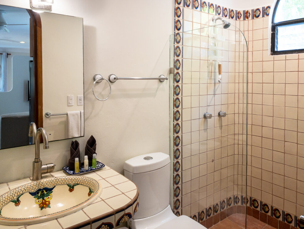 Decorated sink, toilet, and glass-screened tiled shower beneath an arched window.