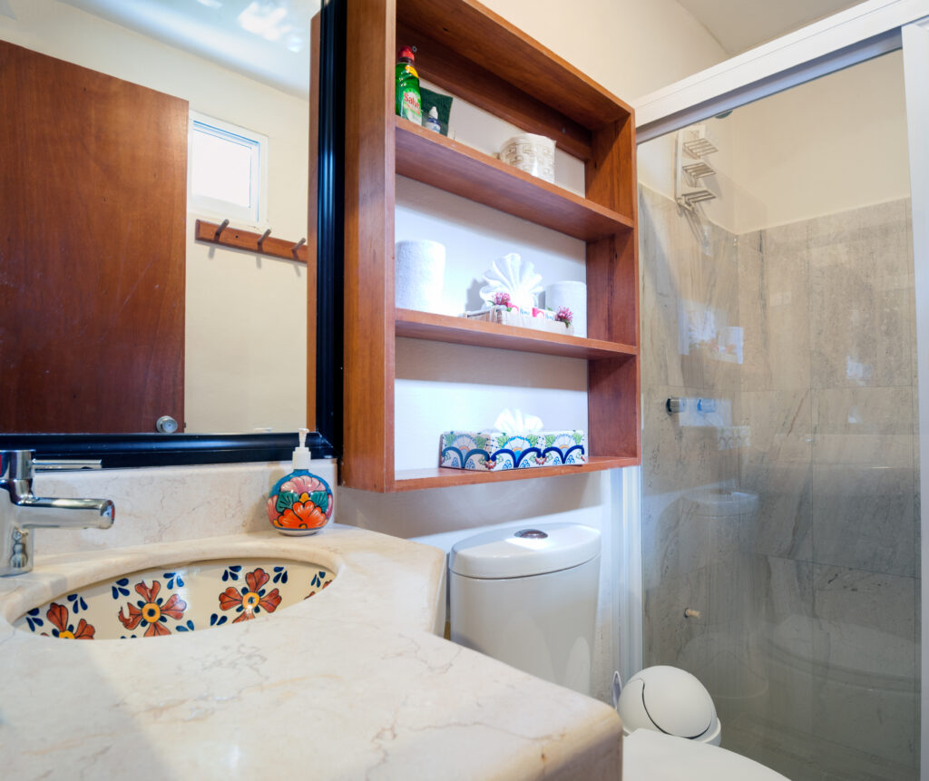 Decorative floral sink beneath a mirror beside open shelves, a toilet, and a shower curtain.