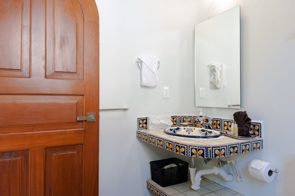 Decorated ceramic sink with a tiled counter beneath a mirror beside an arched wooden door.