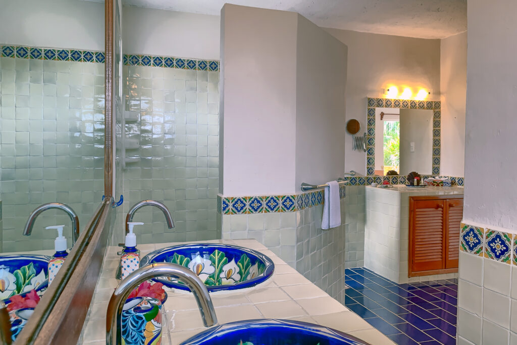 Decorative ceramic sinks beside a tiled shower area and a vanity visible beyond a partition.